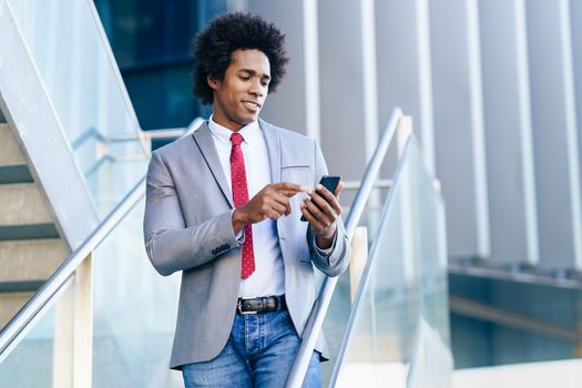 Black Businessman using his smartphone near an office building. Man with afro hair.