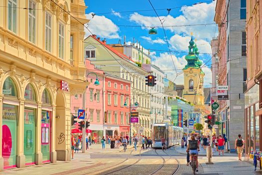 Linz - June 2020, Austria: View through the main street of the city with walking people, shops, tram lines, and a tram