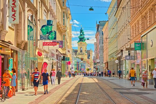 Linz - June 2020, Austria: View through the main street of the city with walking people, shops, and tram lines