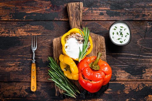 Roast bell pepper stuffed with beef meat, rice and vegetables on a wooden board. Dark wooden background. Top view.