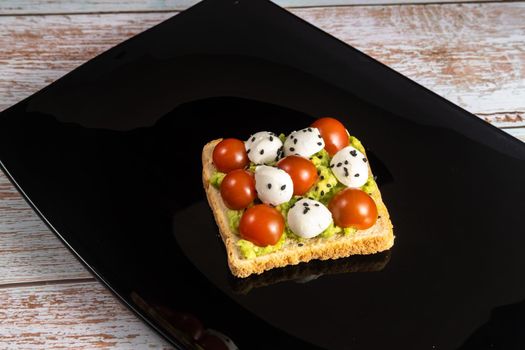 A cheese and tomato sandwich sits in a black plate on a wooden background.