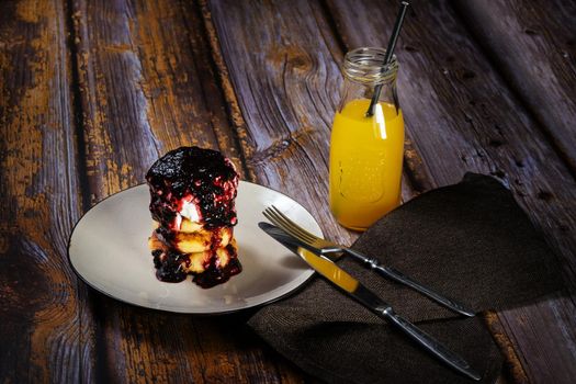 Cheesecakes with blueberry jam and sour cream on a plate with orange juice in a bottle.