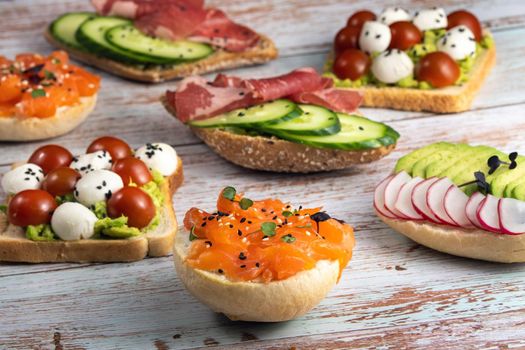 An assortment of sandwiches with fish, cheese, meat and vegetables lay on the wooden table.