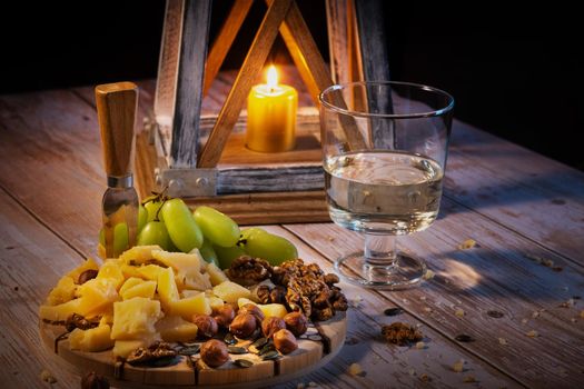 Cheese plate with a variety of snacks on the table with two glasses of wine by candlelight.