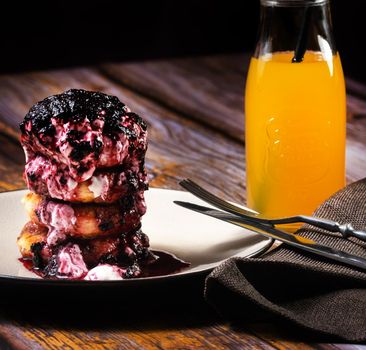 Fried Cheesecakes with blueberry jam and sour cream on a plate with orange juice in a bottle.