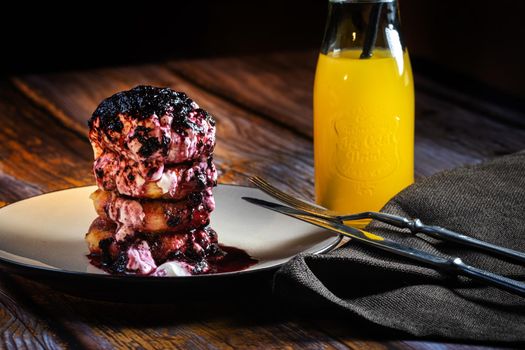 Fried Cheesecakes with blueberry jam and sour cream on a plate with orange juice in a bottle.