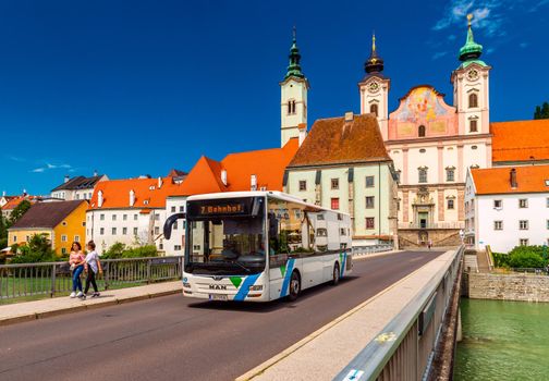 Steyr - June 2020, Austria: View of the Steyr Bridge with a modern bus, walking girls, and St. Michael's Church