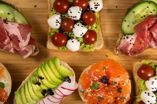 Assorted sandwiches with fish, cheese, meat and vegetables lying on the board.