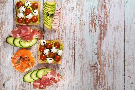 An assortment of sandwiches with fish, cheese, meat and vegetables lay on the wooden table.