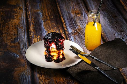 Cheesecakes with blueberry jam and sour cream on a plate with orange juice in a bottle.