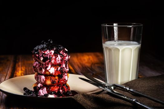 Cheesecakes with blueberry jam and sour cream on a plate with a glass of milk on the table.