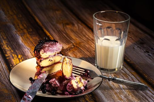 sliced cheesecakes with blueberry jam and sour cream on a plate and a glass of milk on a wooden table.