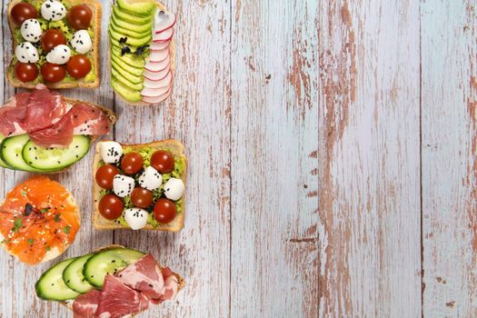 An assortment of sandwiches with fish, cheese, meat and vegetables lay on the wooden table.