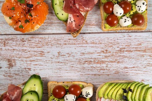 An assortment of sandwiches with fish, cheese, meat and vegetables lay on the wooden table.