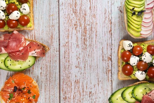 An assortment of sandwiches with fish, cheese, meat and vegetables lay on the wooden table.