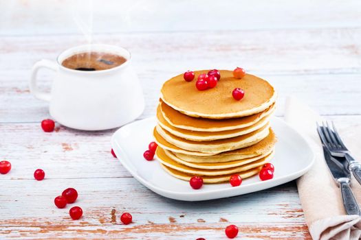 morning breakfast pancakes with cranberries on a wooden table and a cup of coffee.