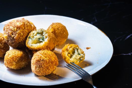 cheese balls with dill inside for a snack in a plate on a black background.