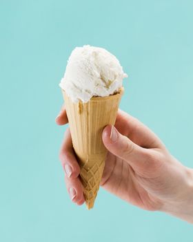 hand holding vanilla ice cream cone blue background
