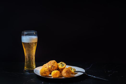 cheese balls with garlic and dill inside for a snack with a glass of beer on a black background.