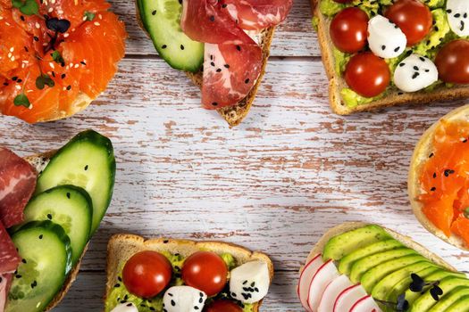 An assortment of sandwiches with fish, cheese, meat and vegetables lay on the wooden table.