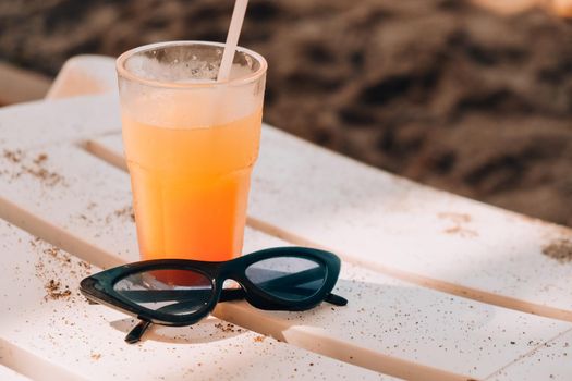 Fresh cold mango smoothie cocktail on tropical beach bright sand. Summer sea vacation and travel concept. Glass of fruit cocktail and sunglasses. Summertime vacation