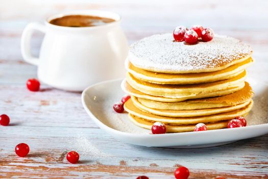 morning breakfast of pancakes with cranberries and powdered sugar on a wooden table and a cup of coffee.