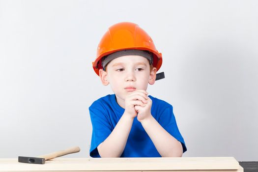 thoughtful boy in a helmet during the construction of a structure of wood, closeup
