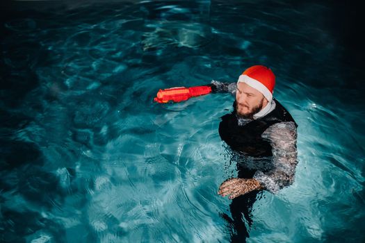 A man in a Santa Claus suit and hat with a red gun in his hands. Santa Claus is swimming underwater with a gun.Christmas concept