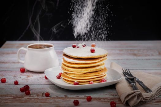 morning breakfast of pancakes with cranberries and powdered sugar on a wooden table and a cup of coffee.