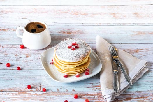 morning breakfast of pancakes with cranberries and powdered sugar on a wooden table and a cup of coffee.