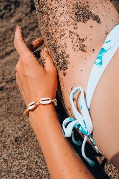 Woman's hands with shell jewelry in sand. Sand in hands on the beach. Travel and vacation concept. Female slim legs. Summertime relax