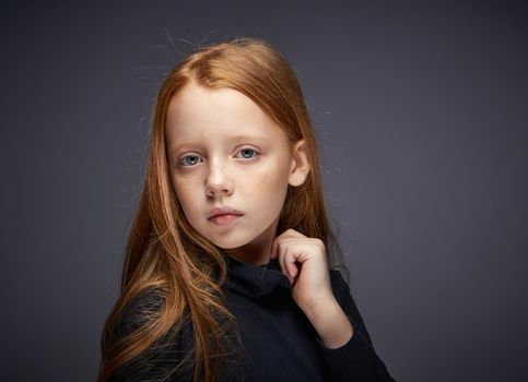 red-haired girl with freckles on her face in a black sweater posing. High quality photo