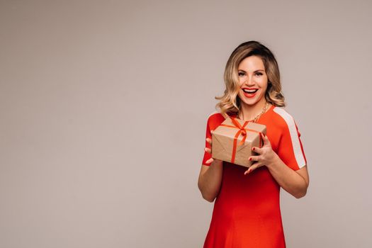 A girl in a red dress stands with gifts in her hands on a gray background.