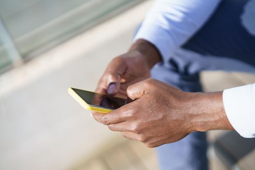 Hands of unrecognizable black man using a smartphone sitting on a urban step.