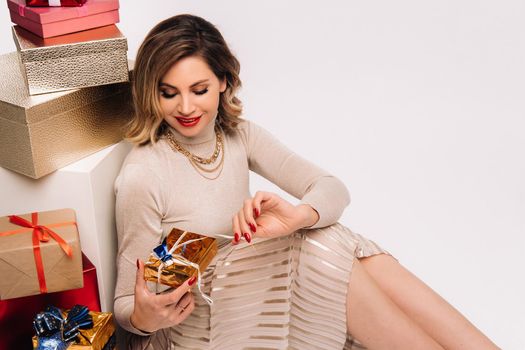 A girl in a skirt and jacket with a bunch of gifts in her hands sits on a white background