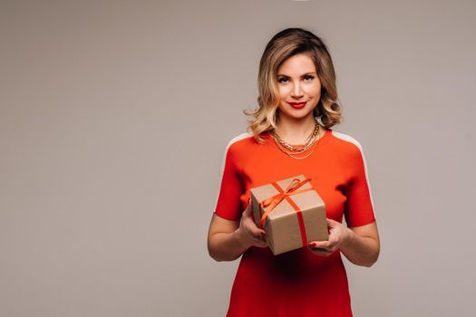 A girl in a red dress stands with gifts in her hands on a gray background.