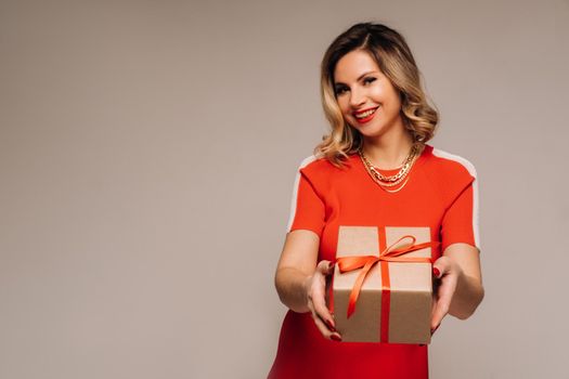 A girl in a red dress stands with gifts in her hands on a gray background.