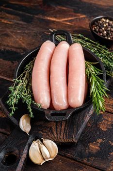 Pork raw sausages in a pan with herbs. Dark wooden background. Top view.