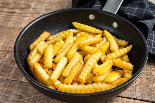 Deep fried Crinkle French fries potatoes sticks in a pan. Wooden background. Top view.