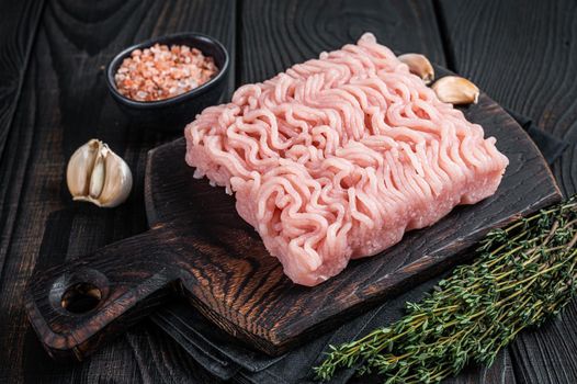 Fresh Raw mince or ground chicken meat on wooden chopping board with thyme. Black wooden background. Top view.