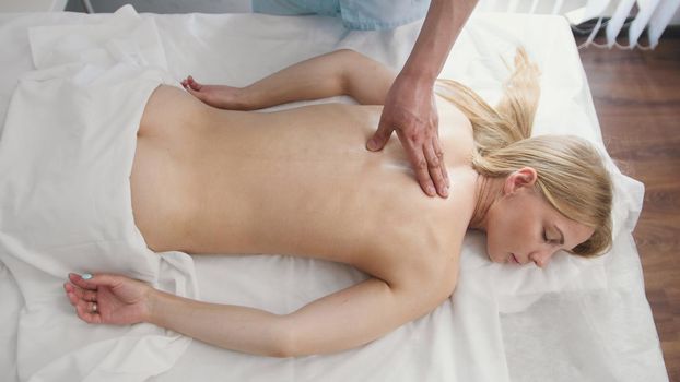 Blonde young woman model in clinic receiving massage for back, top view