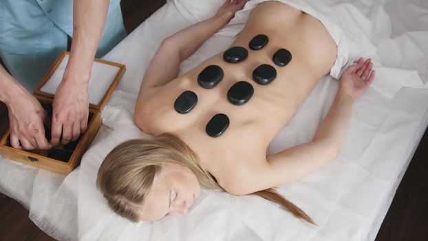 The clinic of Tibetan medicine. The doctor corrects stones for stone therapy on the back girl's