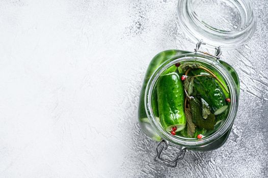 Green pickle cucumbers in a glass jar. Natural product. White background. Top view. Copy space.