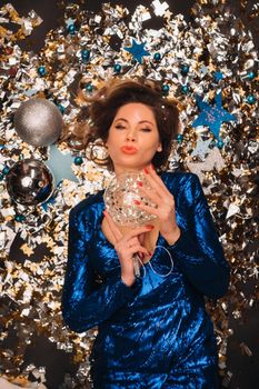 a woman in a blue sequined dress smiles and lies on the floor under a falling multicolored confetti.