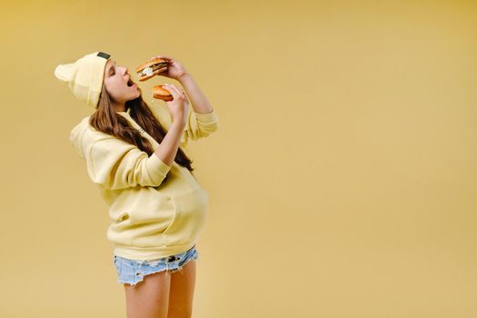 pregnant girl in yellow clothes with hamburgers in her hands on a yellow background.