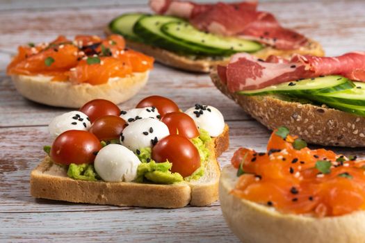 An assortment of sandwiches with fish, cheese, meat and vegetables lay on the wooden table.