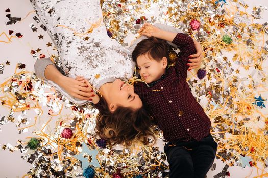 mother and son lie on the floor in confetti on a white background. A woman and a boy in confetti on a white background.