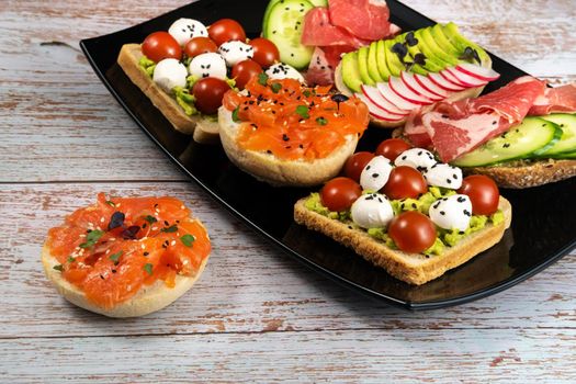 Assorted sandwiches with fish, cheese, meat and vegetables on a black plate.