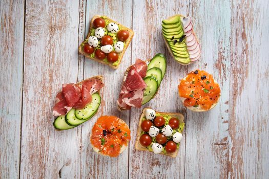 An assortment of sandwiches with fish, cheese, meat and vegetables lay on the wooden table.