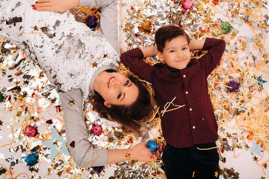 mother and son lie on the floor in confetti on a white background. A woman and a boy in confetti on a white background.